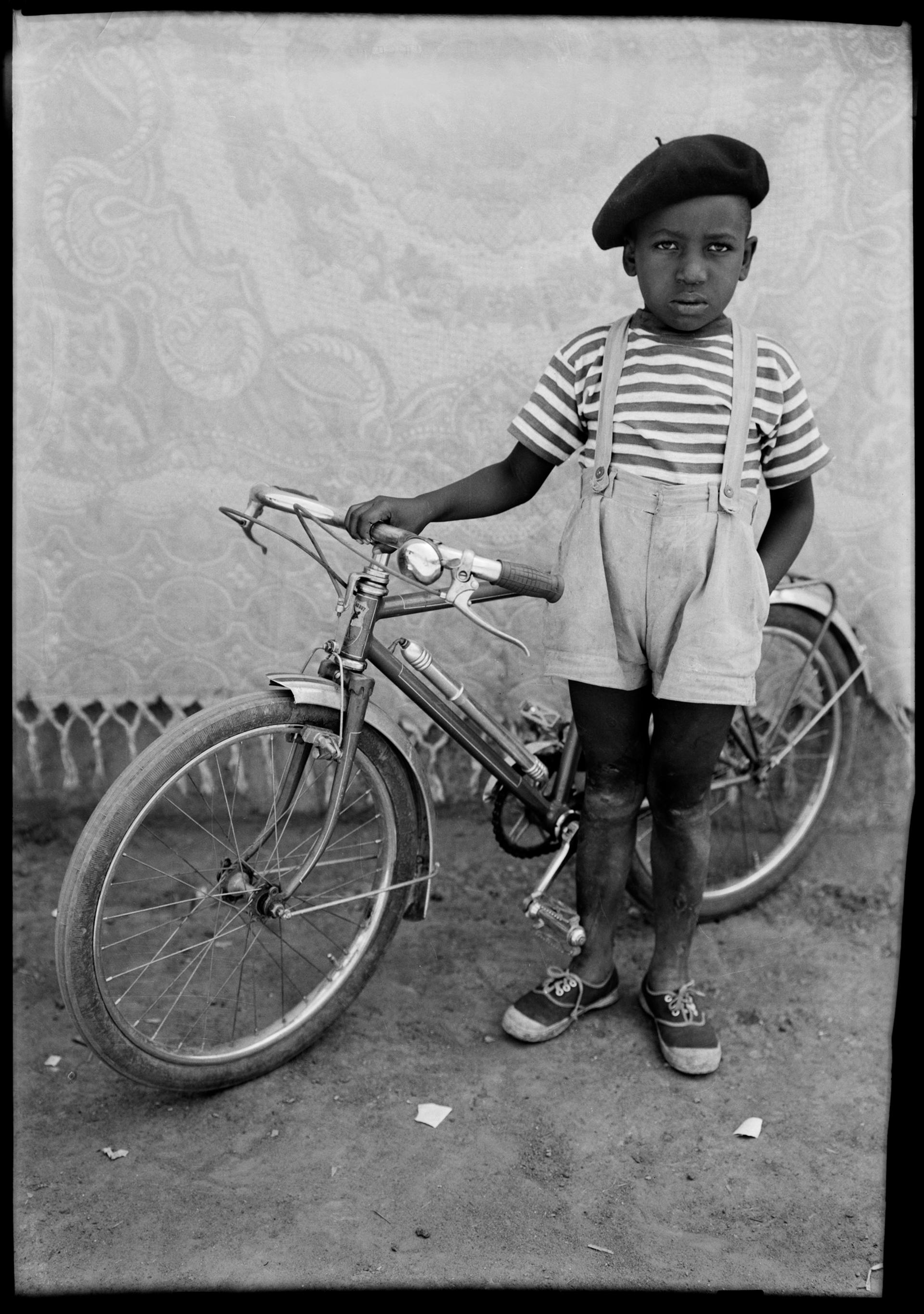 Black-and-white photograph of a child in a beret with a bicycle