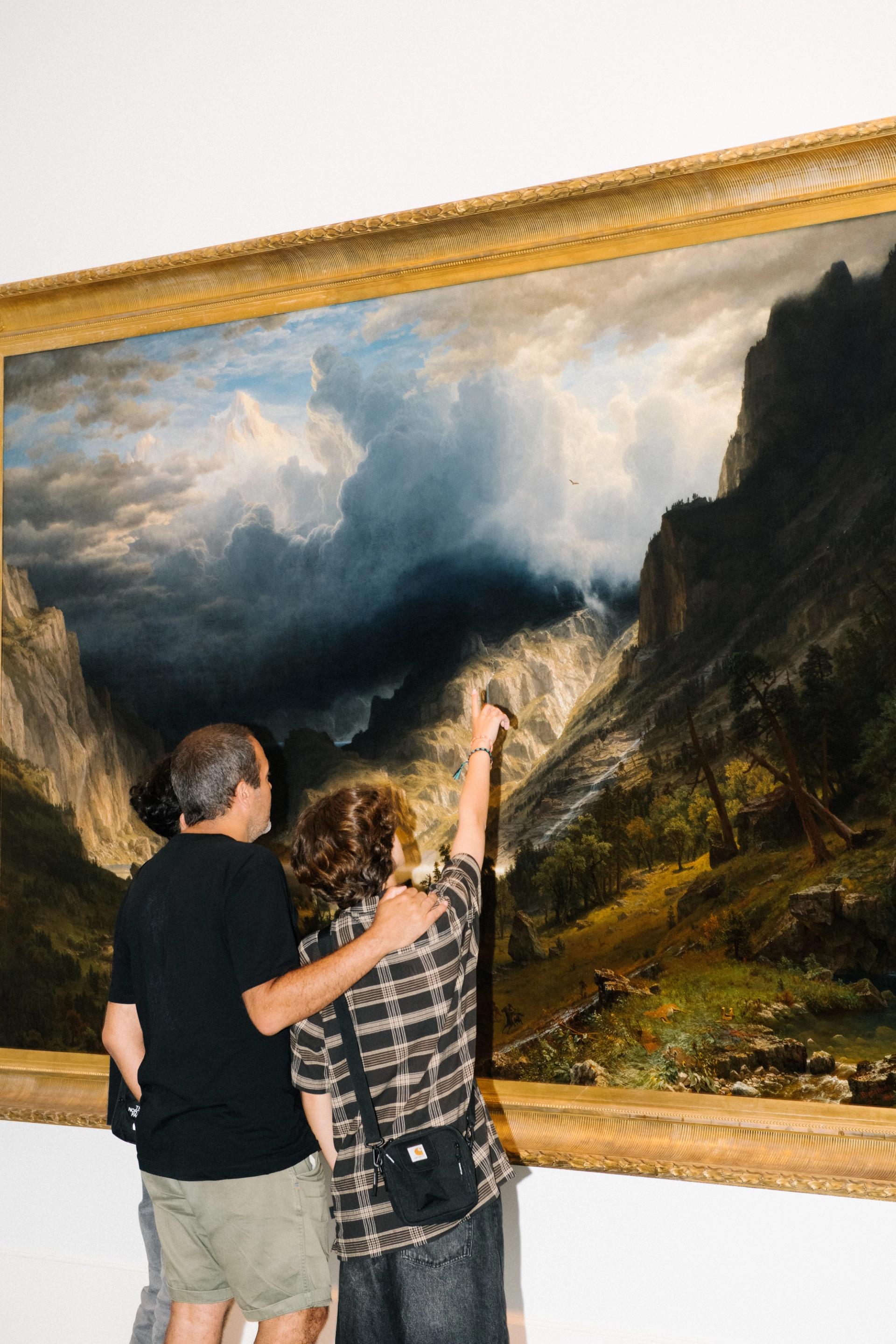 Family of three looks at a large stormy landscape, one of them pointing up towards the clouds